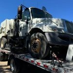 Front-side view of the International street sweeper on its trailer — shipment to Santa Cruz