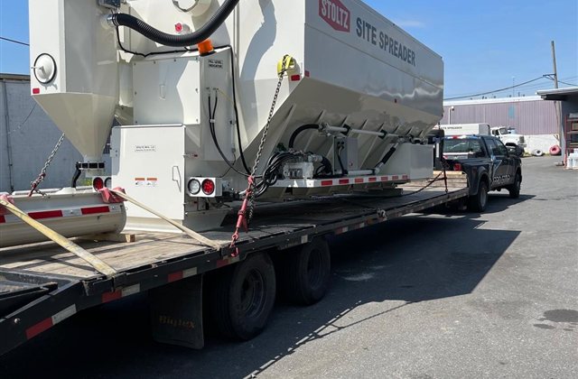 Towable Stoltz Site Spreader — A white Stoltz Site Spreader with its own axle group and towing frame is shown from two angles. View 1.