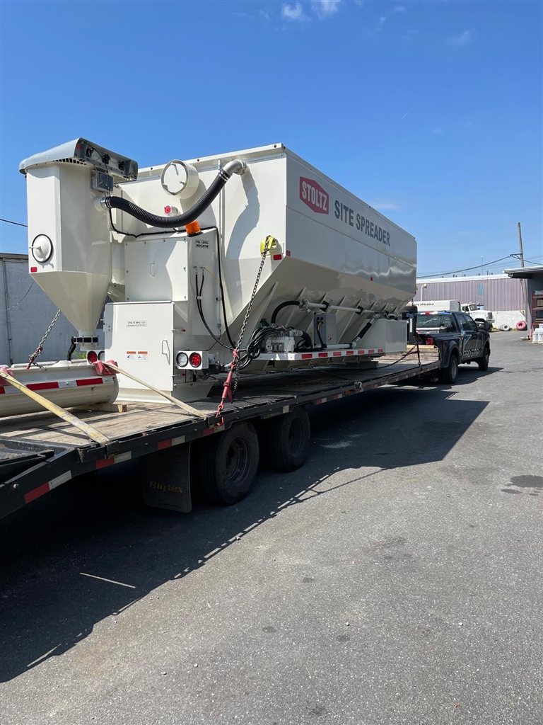 Towable Stoltz Site Spreader — A white Stoltz Site Spreader with its own axle group and towing frame is shown from two angles. View 1.